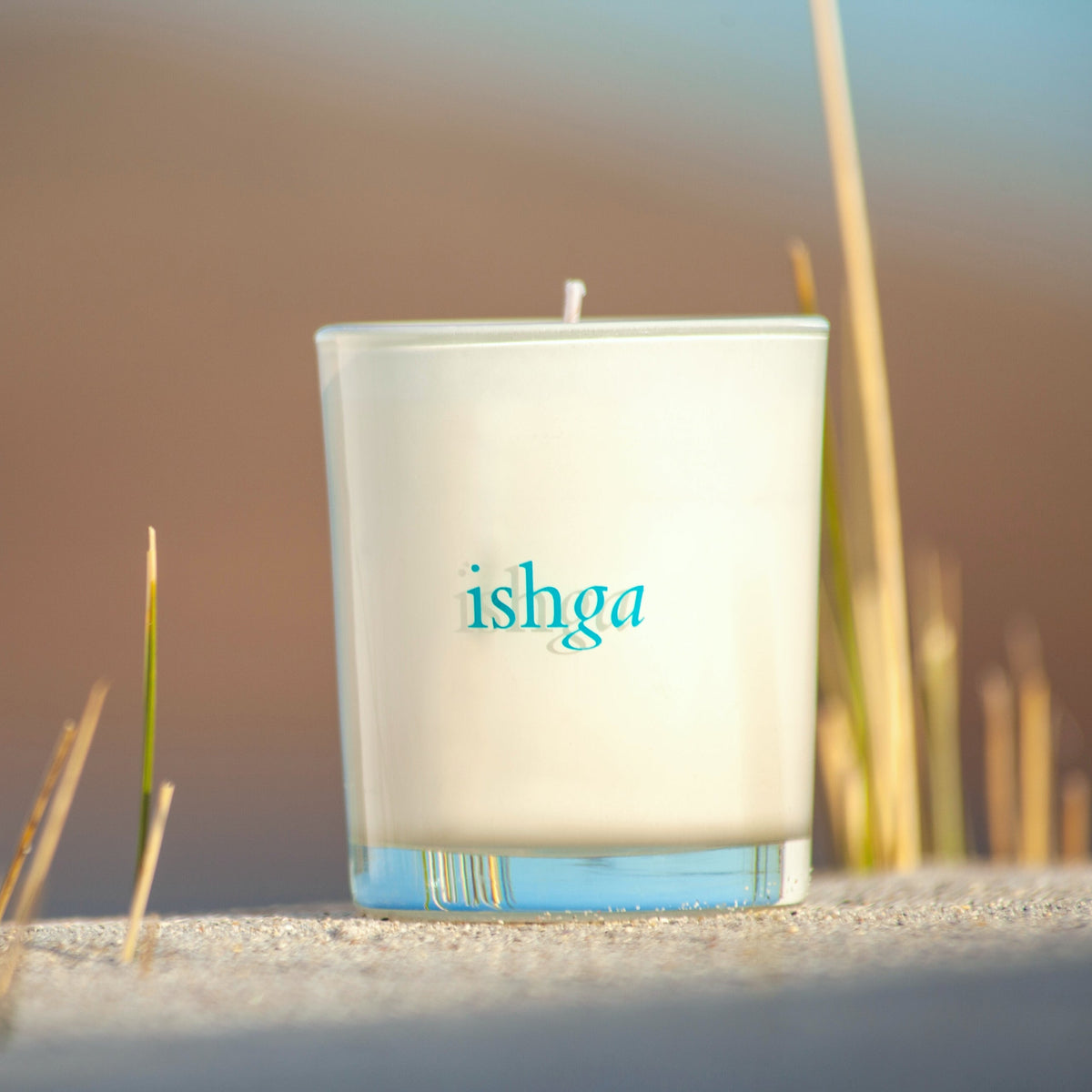 organic soya wax candle jar on beach with sand and grass reeds