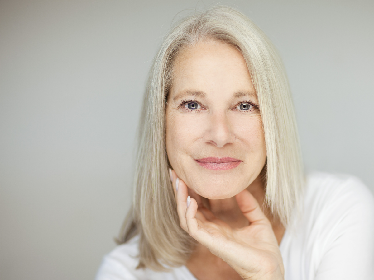 Grey haired lady with her hand under her chin smiles at camera