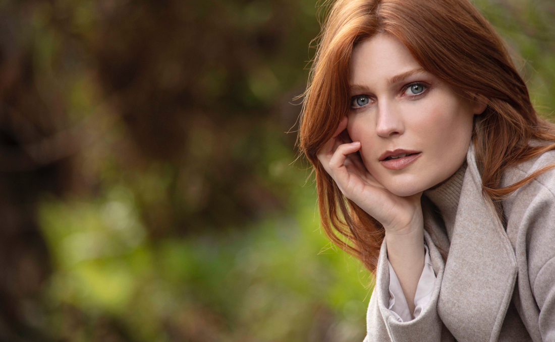 Red haired lady with head resting on her hand looks at the camera