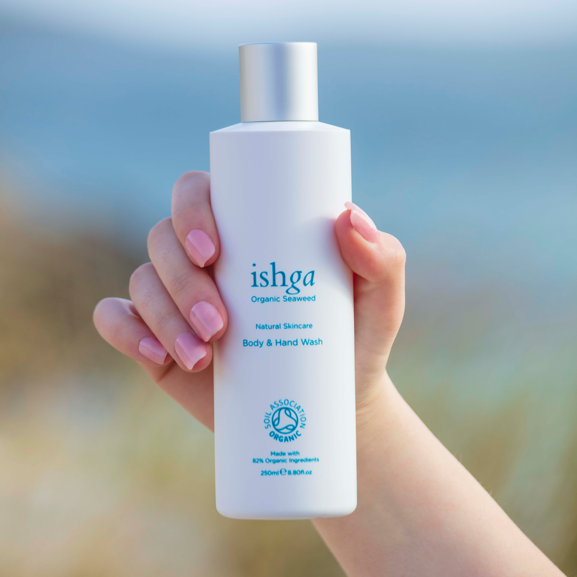 Body and Hand Wash held up with hand against beach background