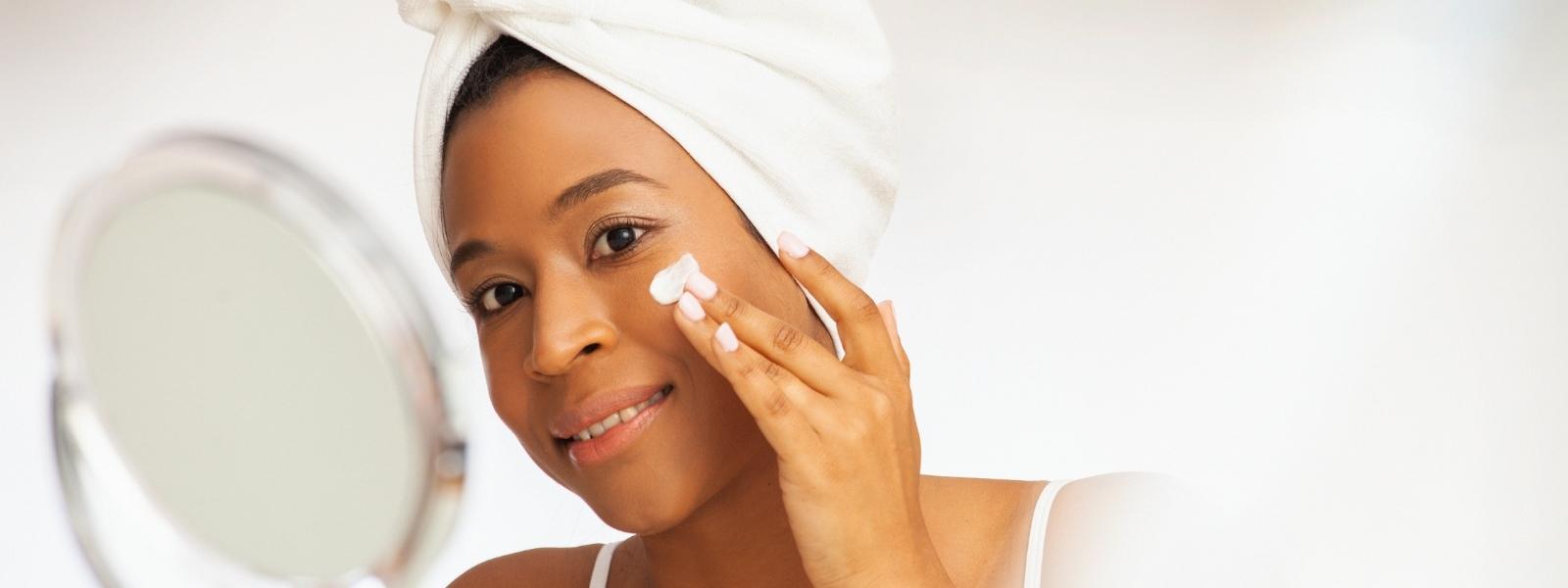 Woman applying skincare with towel on head and mirror in background ishga skincare
