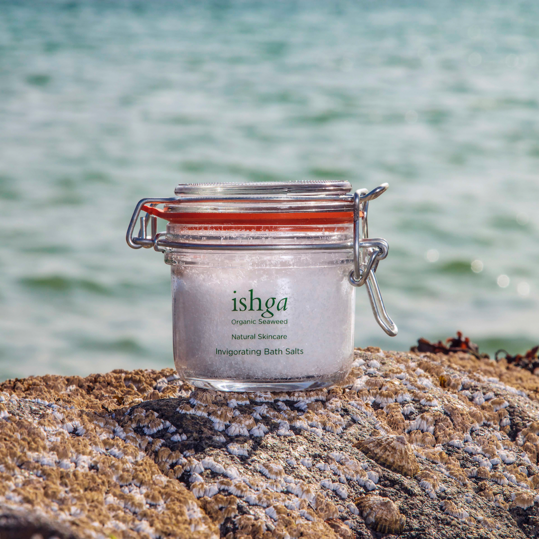 Glass jar of ishga Invigorating Bath Salts on top of rock next to the sea